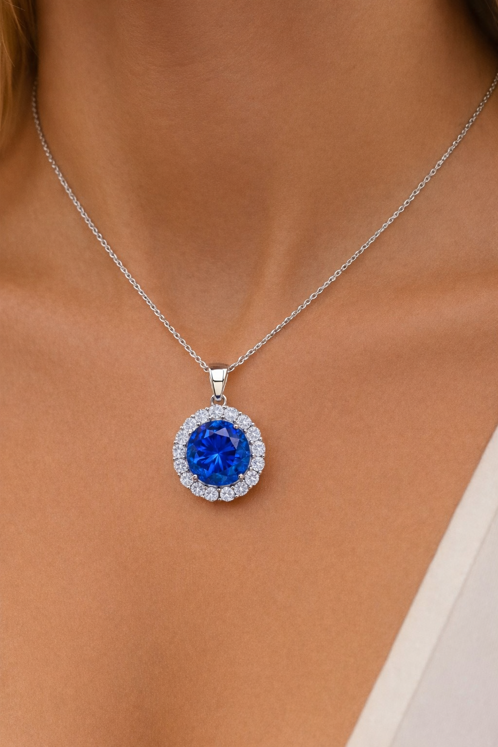 Blue sapphire diamond halo pendant featuring natural royal blue sapphire surrounded by brilliant diamonds set in white gold on model